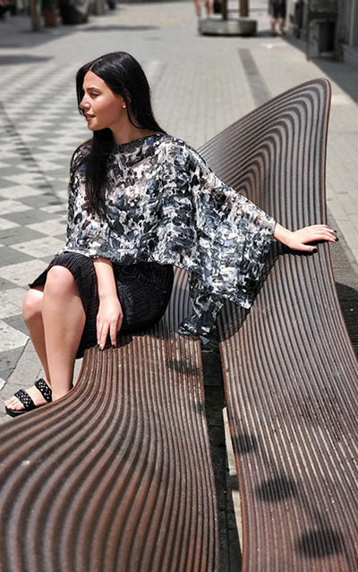 Woman wearing the Garden Path Poncho in Sand Dollar while on a bench. Made in Seattle, WA, USA by Pandemonium Seattle.
