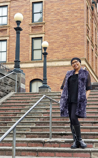 Woman Standing on Stairs in Mandarin Vest Long | Highland in Sky Denim and Gray Faux Fur with Cuddly Black Faux Fur | By Pandemonium Millinery | Handmade in Seattle WA USA