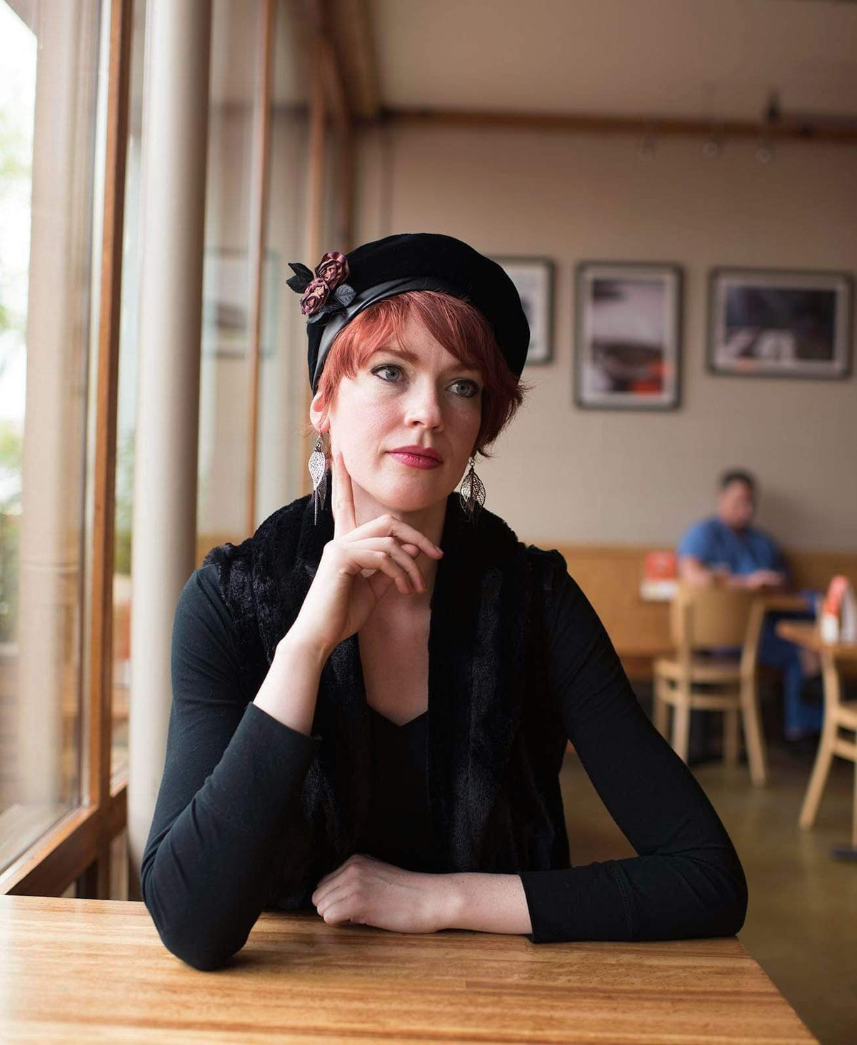 Model sitting in Coffee Shop wearing a Velvet in Black Beret with a Rose Brooch | Pandemonium Millinery| Handmade in Seattle WA