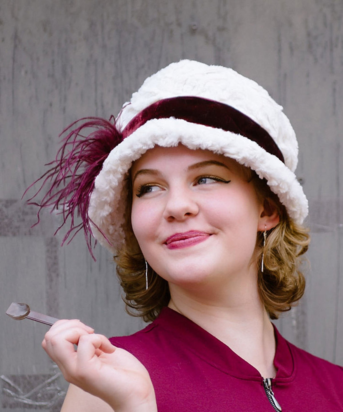  Model wearing Grace 1920s Cloche Style Hat in Cuddly Faux Fur Ivory featuring Midori Velvet  Crimson Band  with Burgundy Ostrich Feather Brooch | Handmade By Pandemonium Seattle | Seattle WA USA