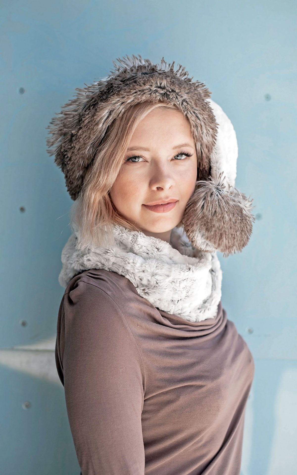 Model against blue wall is wearing a Neck Warmer and matching Santa Hat | Winter's Frost White and Faint Black spots Faux Fur | Handmade in the USA by Pandemonium Seattle