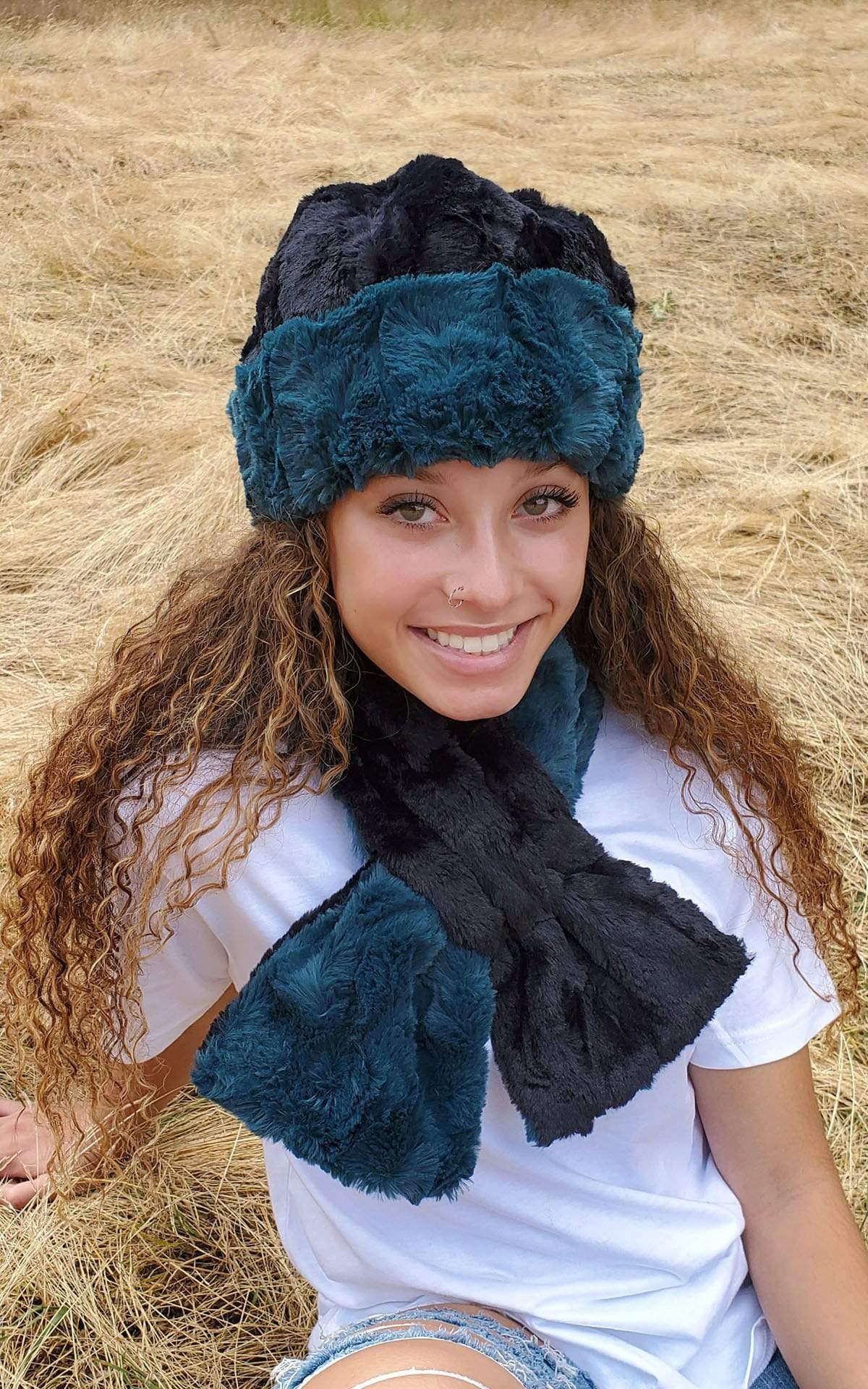  Model sitting in field wearing a Beanie and a matching  Women’s Pull Through Scarf shown in reverse Peacock Pond Faux Fur, Blue / Teal with Cuddly Faux Fur in Black | Handmade in Seattle WA | Pandemonium Millinery