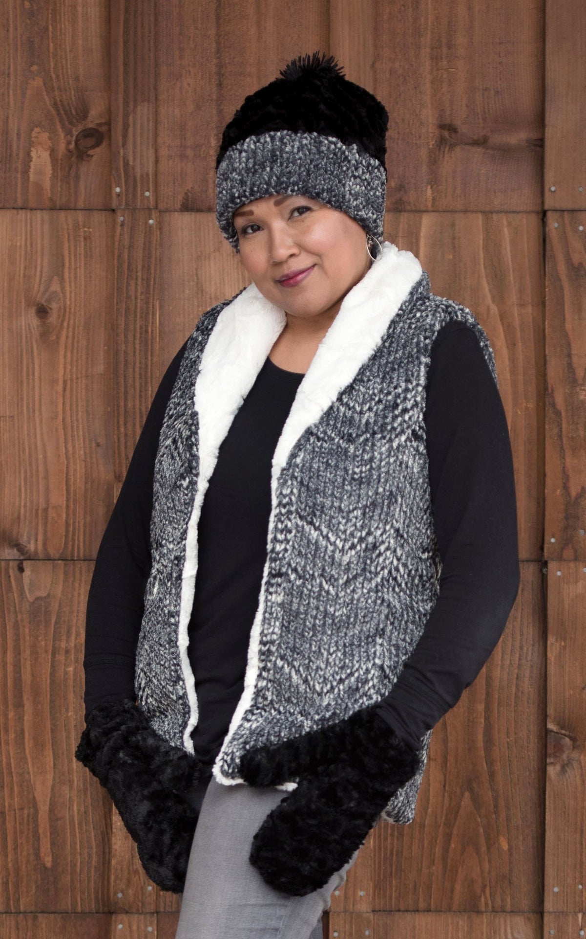 Model against a wood wall wearing Shawl Collar Vest | Cozy Cable in Ash Faux Fur  with Matching Beanie  | Handmade In Seattle WA | Pandemonium Millinery