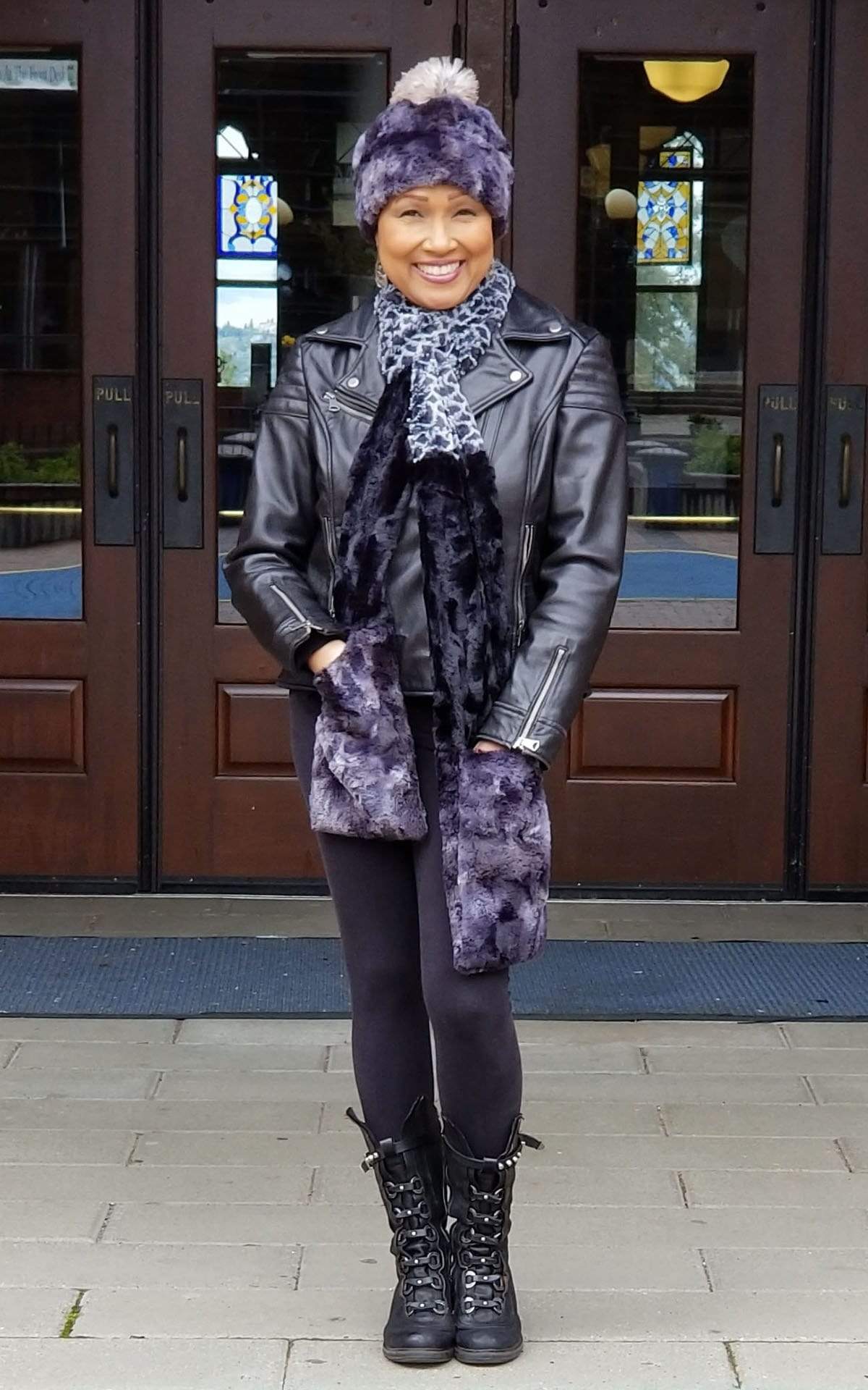 Women in front of Glass and wood doors wearing Beanie hat with Pom Pom with matching  the Color Tri-Color Pocket Scarf | Snow Owl, Cuddly Black, and Highland in Skye a  combo of blacks grays, and blue Faux Fur | Handmade in Seattle WA Pandemonium Millinery