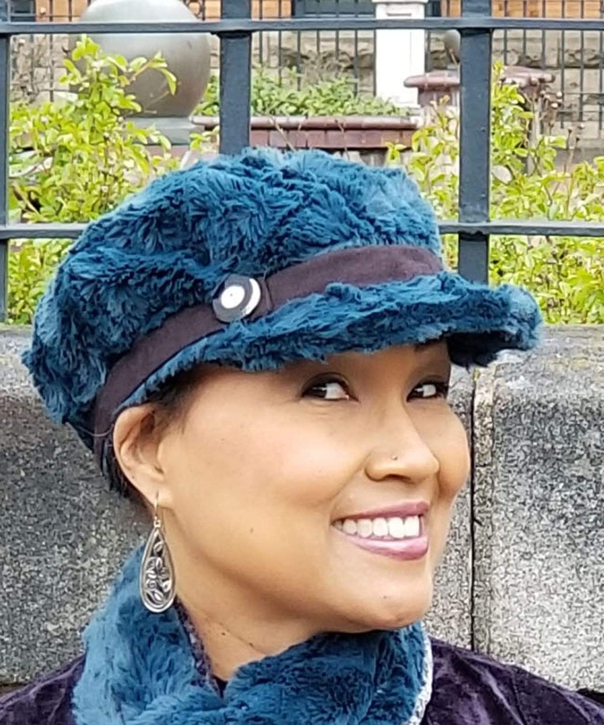  Side View of model wearing a Valerie Cap Style hat in Peacock Pond Faux Fur with Black Faux Suede band and glass button trim By Pandemonium Millinery. Hand made in Seattle, WA USA.